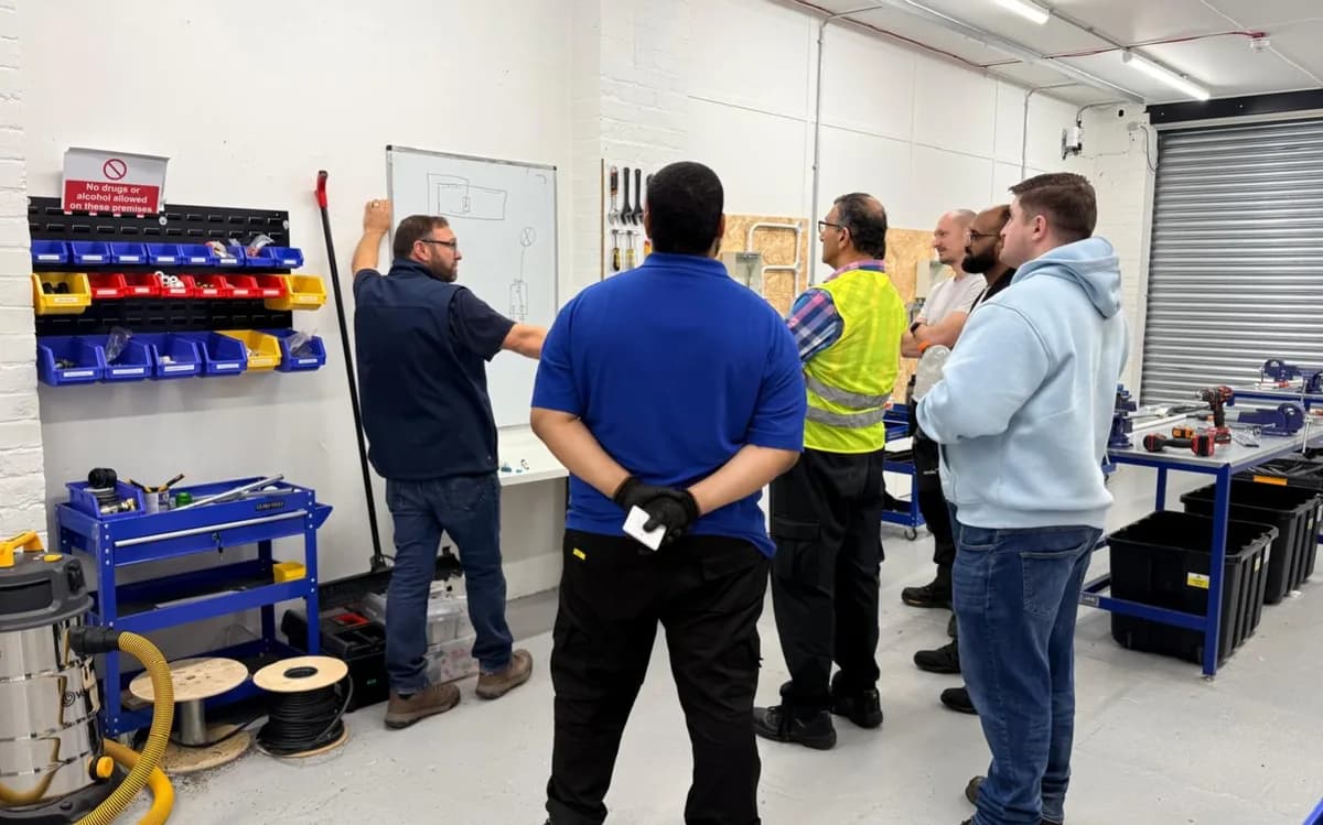 Electricians training at workbenches with diagnostic equipment and tools in an industrial workshop setting.