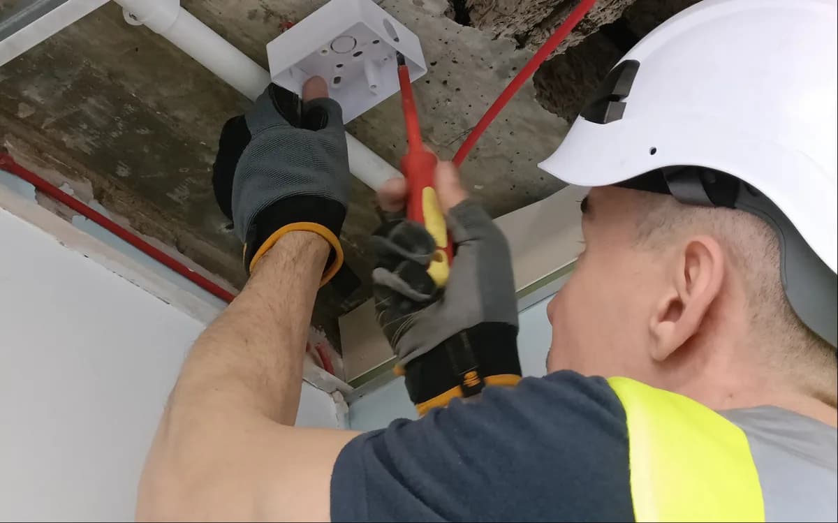 Electrician's hand testing circuit breakers and wiring in industrial electrical panel with colored cables.
