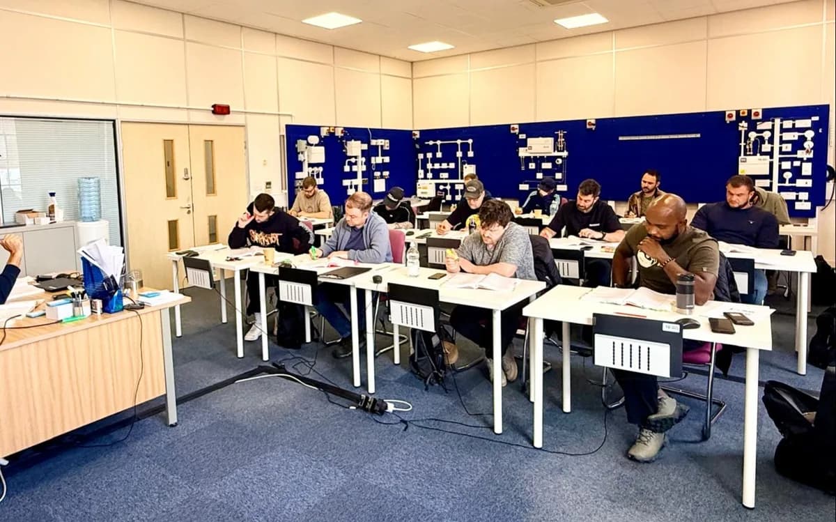 Students work at individual computer stations in a modern electrical training classroom with brick walls and large windows.